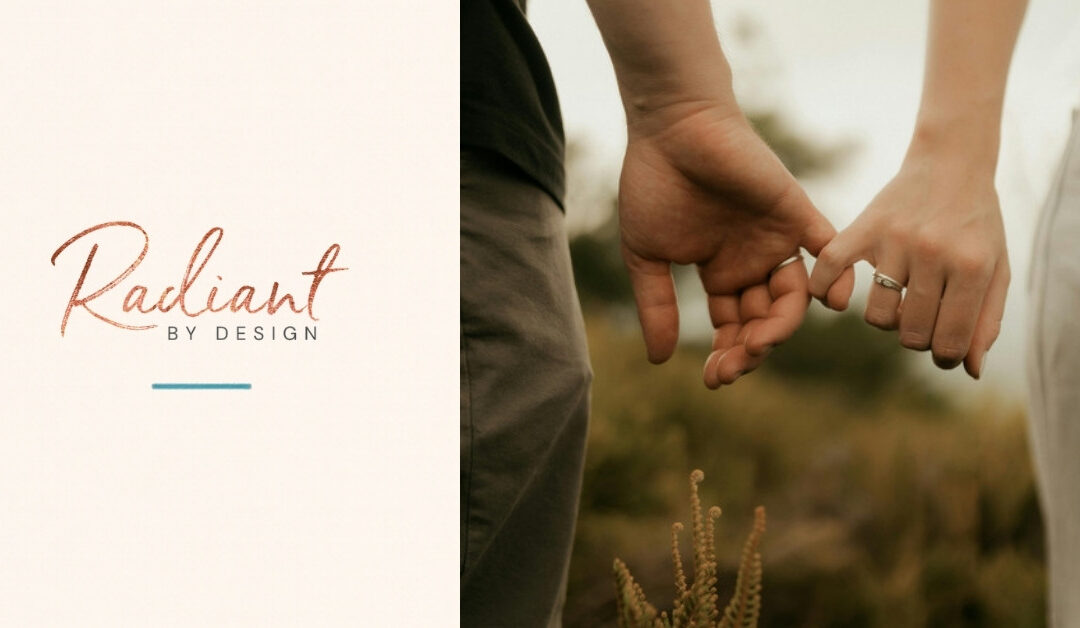 Two people wearing rings link pinky fingers outdoors against a soft, blurred background of greenery.