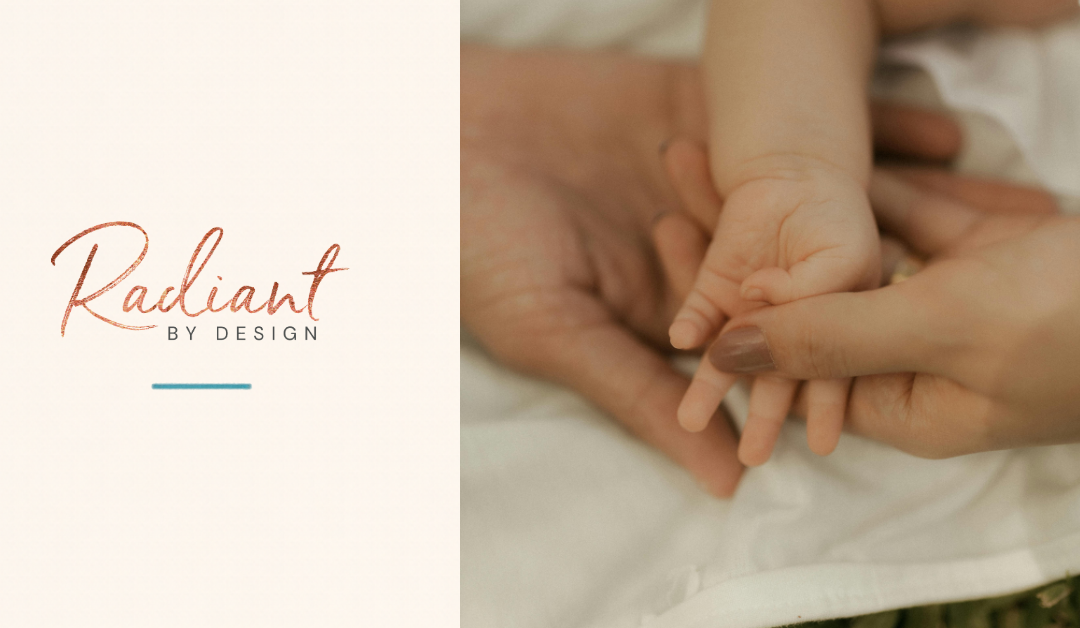 A baby's tiny hand rests in a parent's open palm, held gently by another adult hand on white fabric.