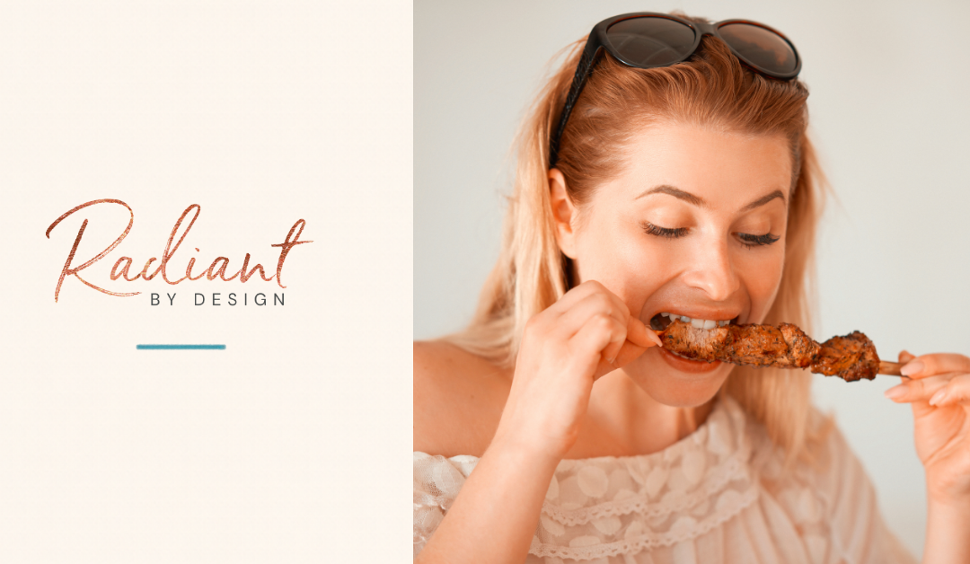 A smiling blonde woman with sunglasses on her head bites a piece of grilled meat from a skewer.