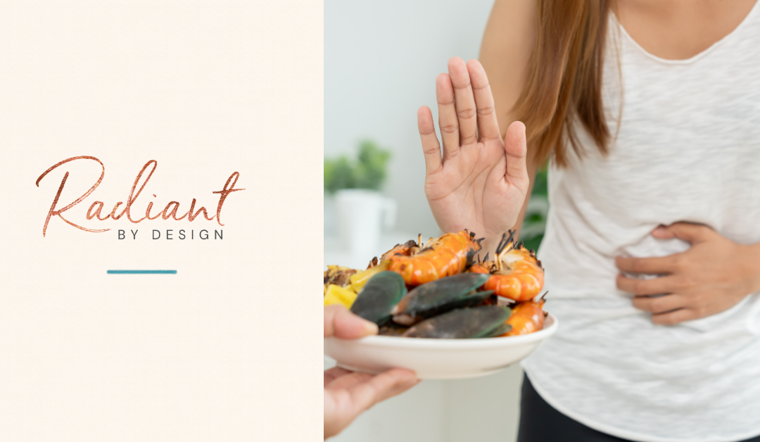 A woman in a gray tank top holds one hand up to refuse a plate of shrimp and mussels while the other hand rests on her stomach.